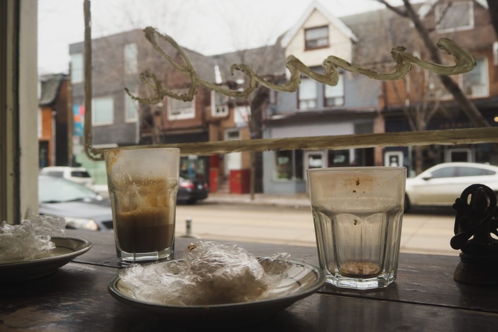 A close-up of two empty coffees and plates on a wooden counter surface and facing out onto a street scene.