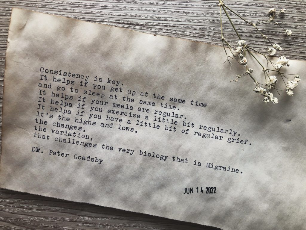 A close up photograph of typewritten text on vintage looking paper, and a sprig of dried baby's breath in top corner. It is an excerpt from a talk by Dr. Peter Gaodsby on Consistency & the Migraine Brain. The full text is contained in the post.