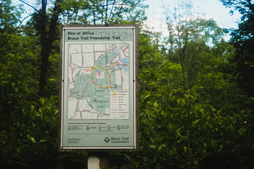 Terrace Creek Short Loop Trail. A photograph of the trail map on a signpost with lush green forest in the background. The title of the map reads: "Rim of Africa, Bruce Trail Friendship Trail."