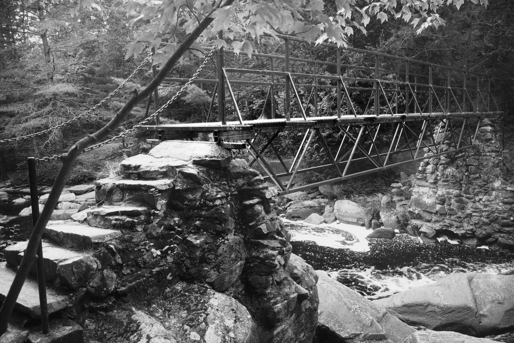 Black and white photo of a bridge crossing the river at Duchesnay Falls hiking trail.