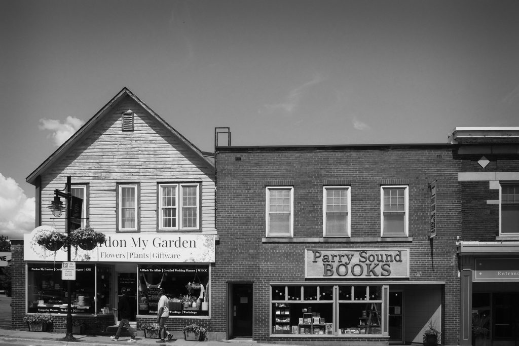 A black and white street view photo of Pardon My Garden and Parry Sound Books.